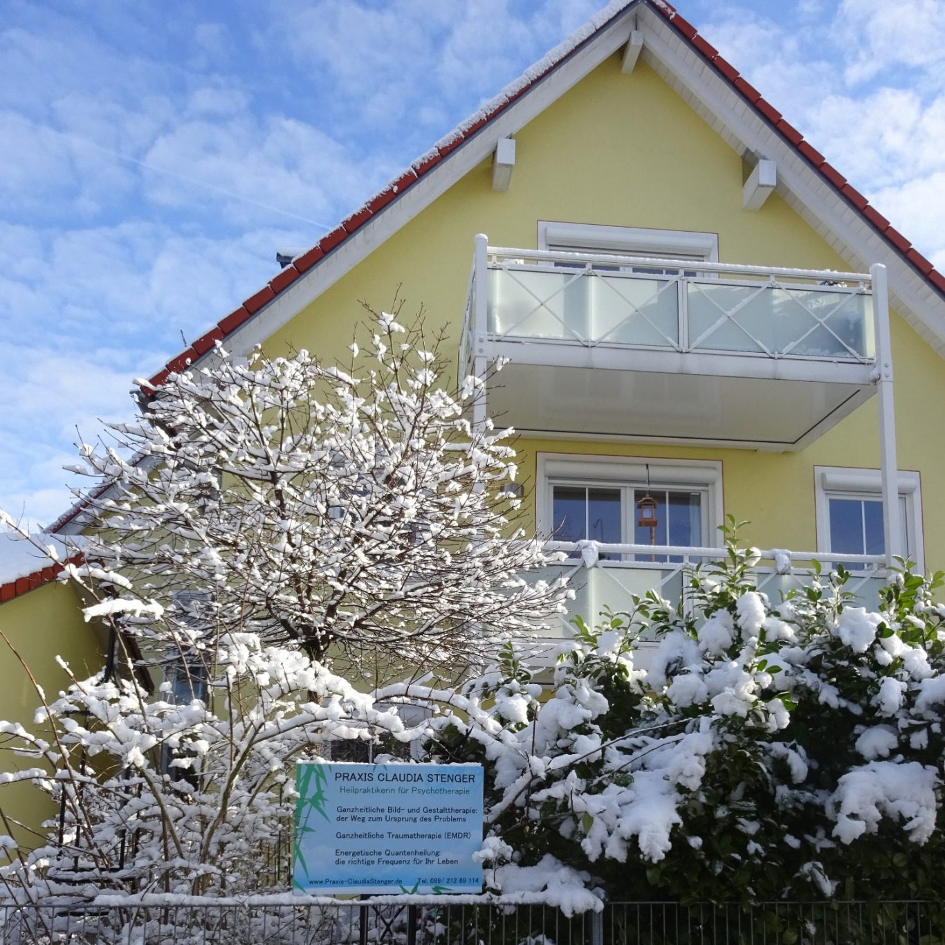Gelbes Haus mit Balkon, umgeben von schneebedeckten Bäumen und Sträuchern.
