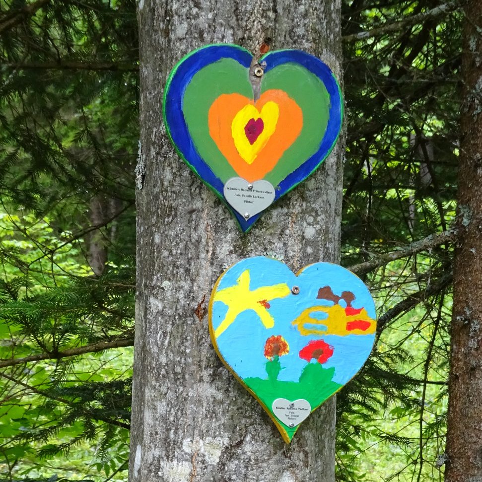 Bunte Herzformen mit einfachen Zeichnungen von Tieren und Pflanzen an einem Baum.