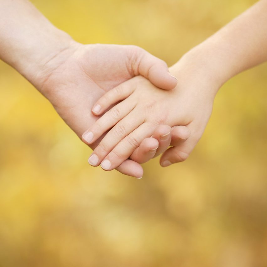 Hände eines Erwachsenen und eines Kindes halten sich vor einem goldenen Hintergrund als Symbol für Versöhnung nach einem Konflikt.