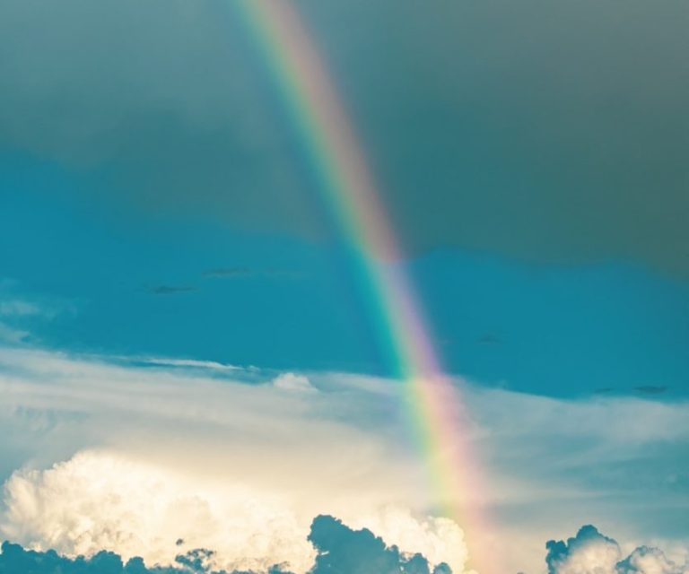 Blick auf einen Berg mit Regenbogen und einem Dorf im Vordergrund.