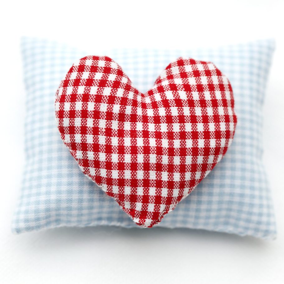 Ein quadratisches Kissen mit rotem, kariertem Herz auf blauer, kariertem Unterlage.