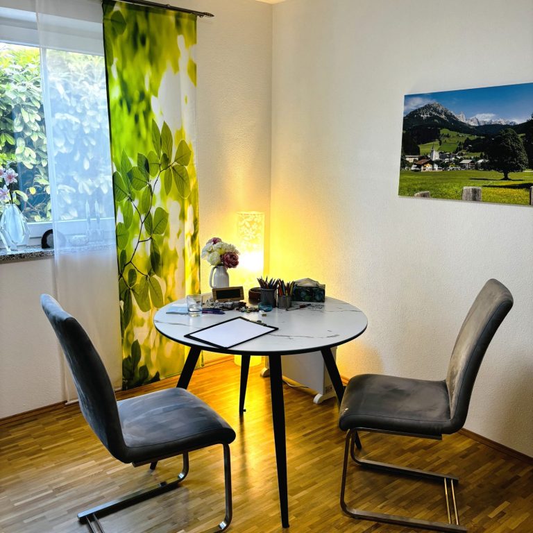 Ein runder Tisch mit zwei Stühlen, Buntstiften und einem Landschaftsbild an der Wand.