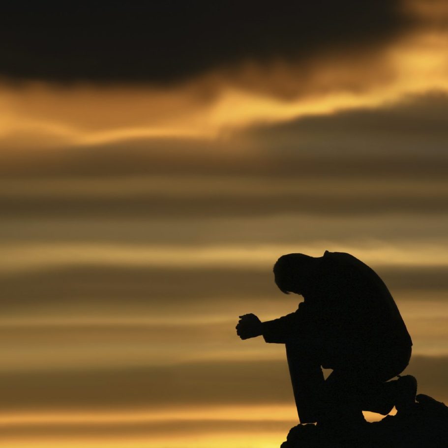 Silhouette einer Person, die in einem emotionalen Moment auf einem Felsen kniet.
