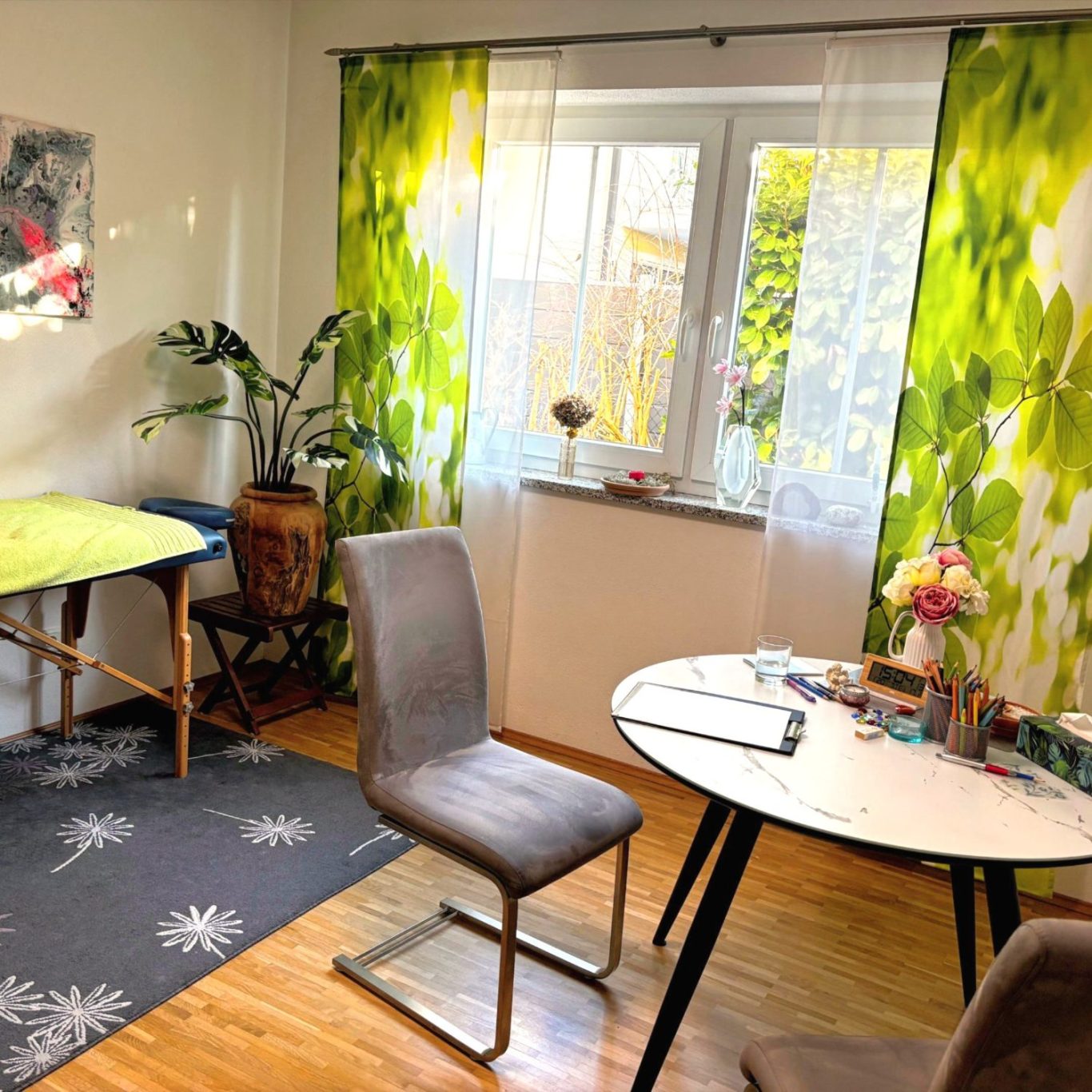 Therapieraum mit grünen Vorhängen, einem runden Tisch mit zwei Stühlen.